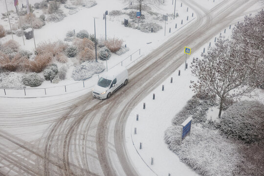 A car approaches a crossroad during snowy conditions. The scene is captured from a height. Slippery roads and zebra crossing ahead. 