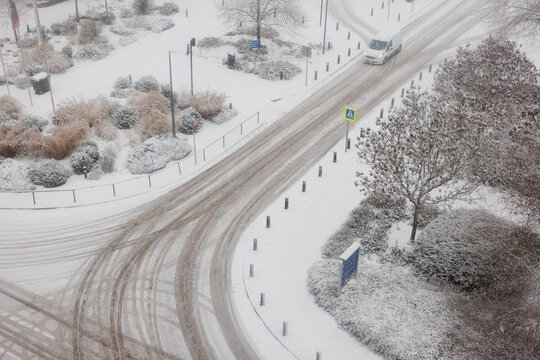 A car approaches a crossroad during snowy conditions. The scene is captured from a height. Slippery roads and zebra crossing ahead. 