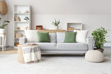 Interior of stylish living room with grey sofa, wicker coffee table and shelving unit