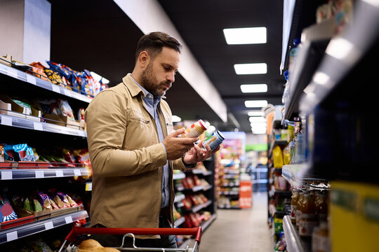 Mid adult man hesitating while choosing baby food in supermarket.