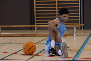 Obraz premium Male athlete sitting on court holding knee, blue uniform, climbing bars and basketball, copy space