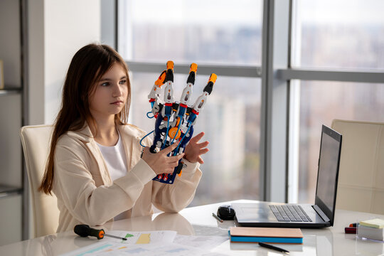 Young woman holding and examining robotic hand. STEAM education