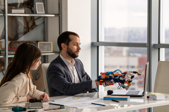 man and woman are working on student project involving robotic arm.