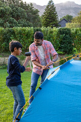 Indian father and son assembling blue camping tent in backyard using poles stakes, rubber mallet © wavebreak3