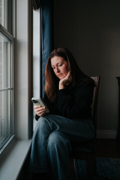 Woman sitting on chair in dark room looking at smartphone.