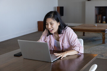 Naklejka premium Asian woman sitting at table typing on laptop and checking smartphone at home