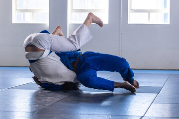 Diverse male training partners grappling, throwing on dojo mats wearing white and blue gis