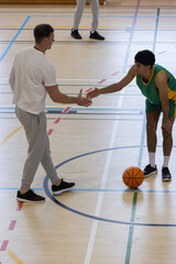 Obraz premium Adult coach shaking hands while african american player holding basketball in uniform on court