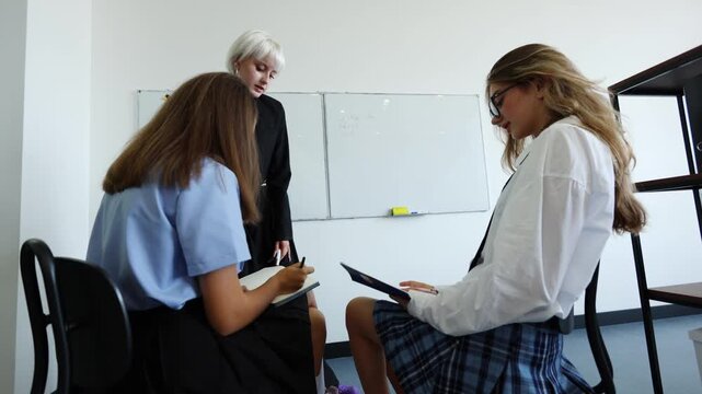 A teacher in black guides two students at a whiteboard, fostering active learning and personalized instruction in a bright, modern classroom setting.