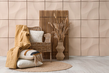 Interior of room with wicker armchair and folding screen near beige tile wall