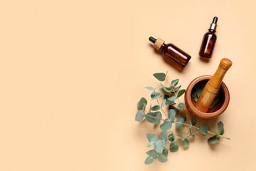 Wooden mortar and pestle with eucalyptus branch and bottles of essential oil on beige background