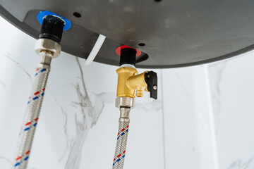 Brass Valve And Braided Hoses Under Water Heater, Clear View Of Inlet And Outlet Fittings On Tiled Wall, Clean Installation Detail Suitable For Plumbing, HVAC, And Smart Home Upgrade Visuals