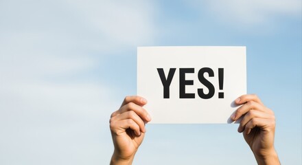 Enthusiastic Affirmation: Person Holding a 'YES' Sign Against a Bright Blue Sky, Symbolizing Approval and Agreement