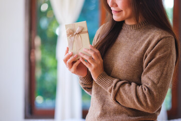 Closeup image of a woman in sweater holding and looking at a present box at home