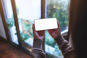 Mockup image of a woman holding mobile phone with blank desktop screen at home