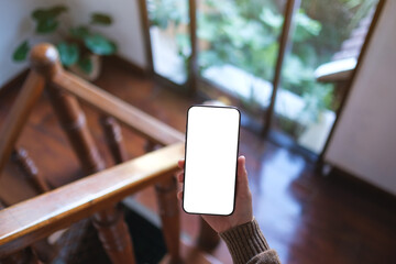 Top view mockup image of a woman holding mobile phone with blank desktop screen at home