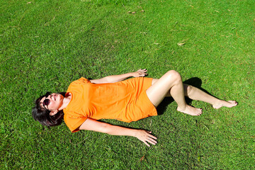 A woman in an orange dress lies on green grass on a sunny day.