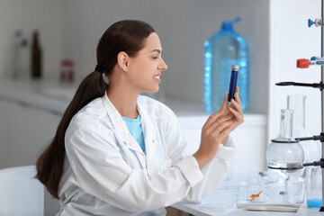 Happy female young scientist with professional glassware examining water quality in research laboratory