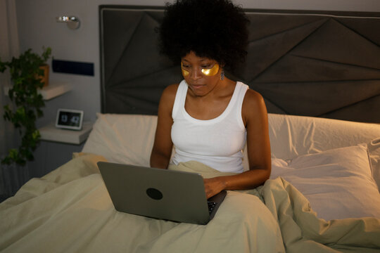 Woman using laptop in bedroom bed during morning self care routine