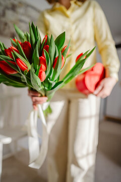 Woman indoors holding tulip bouquet and heart shaped gift box