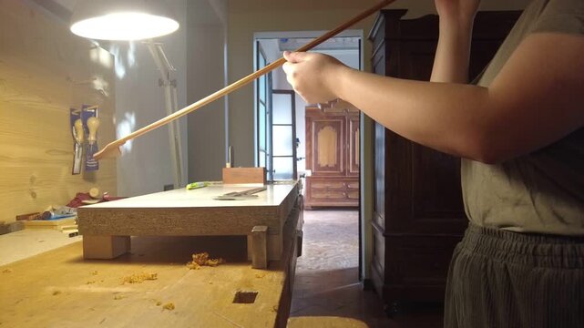 Artisan crafting a violin bow, shaping wood with precision tools in a workshop
