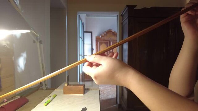 Crafting a violin bow: hands shaping wood with precision tools