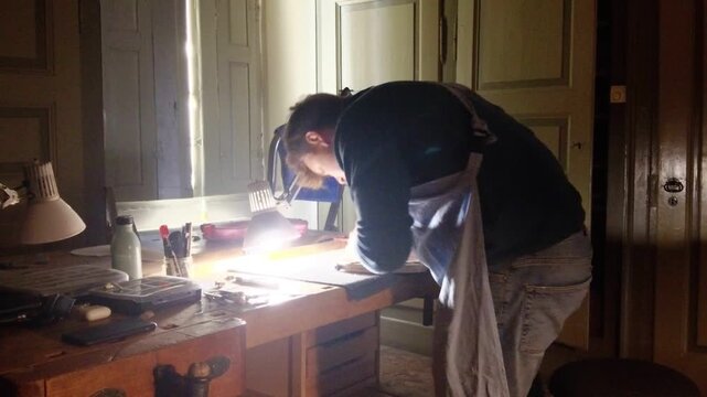 A craftsman focused on detail, working on a wooden body under bright workshop lights, embodying the art of luthiery