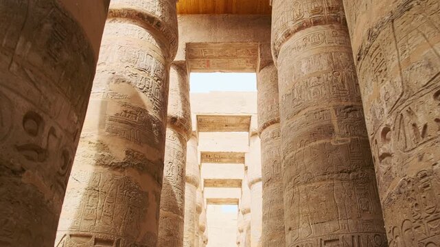 Low angle view of massive stone pillars decorated with ancient hieroglyphs and carvings inside ancient Egyptian temple. Temple of Amun-Ra, Luxor, Egypt. UNESCO World heritage site
