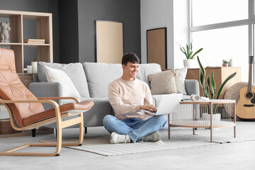 Fototapeta premium Young man using laptop on floor at home
