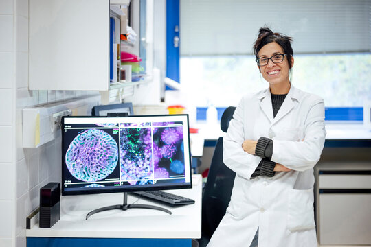 Scientist in lab coat standing by monitor displaying cell images in laboratory
