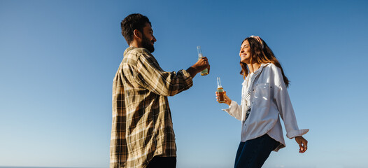 A toast to the day: A couple tapping bottles under an open sky