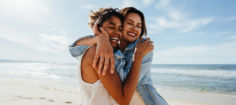 Two friends hugging and smiling together at the beach on a sunny day