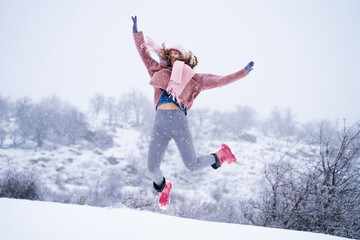 Full length of a happy joyful woman jumping in the winter mountain landscape, walking in snowy nature, enjoying the moment and freedom, winter holidays