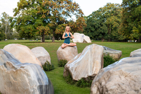 Yoga lotus pose on large rock in park surrounded by nature