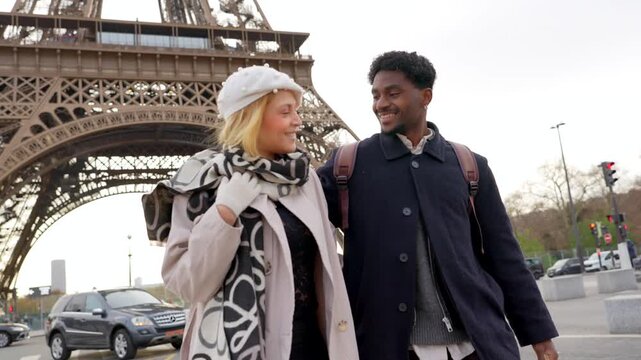 Happy interracial couple enjoying a romantic stroll in paris, walking together arm in arm and smiling with the iconic eiffel tower in the background during their european vacation