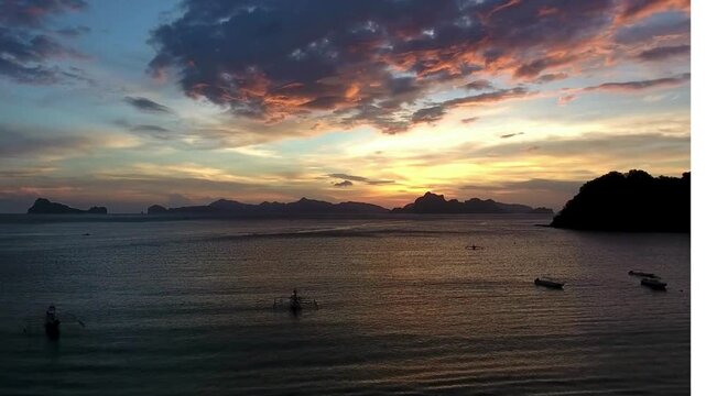A peaceful evening view of a tropical bay at sunset. Several traditional outrigger boats rest on the calm, reflective surface of the water,. Tropical Coastal Sunset with Traditional Outrigger Boats an