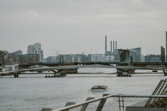 Overcast river bridge connects city waterfront with urban industry smokestack on skyline showing transport links and muted industrial mood