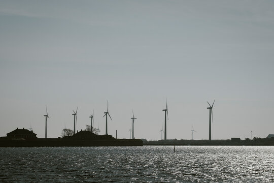 Wind turbine renewable energy on sea horizon with coastline silhouette in changing weather creates open landscape for clean power concept and mood