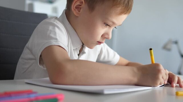 Close-up of a young boy writing or drawing with a pencil at a desk at home or school. Child focused on learning and doing homework. Concept of education, childhood development, concentration