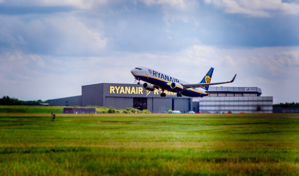 LONDON STANSTED AIRPORT, ESSEX / UK - CIRCA JULY, 2019: Ryanair Boeing 737 takes off with visible Ryanair hangar in background