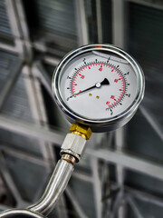 Pressure gauge shows reading in industrial setting with metal pipes and structure in background during daytime