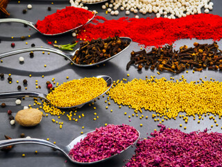 Various spices arranged on spoons with colorful powders and seeds on a surface in a kitchen setting during the daytime