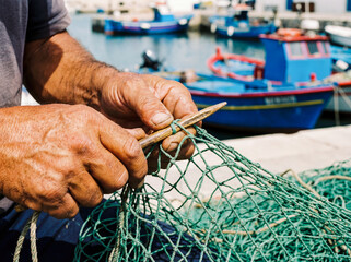 Fisherman mending green nets in port traditional maritime lifestyle manual labor background copy space sicily italy authentic village sea