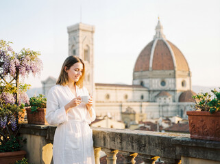 Obraz premium Young woman relaxing on balcony with morning coffee and city view lifestyle travel vacation background copy space florence italy architecture