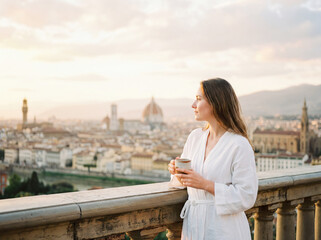 Obraz premium Young woman relaxing on balcony with morning coffee and city view lifestyle travel vacation background copy space florence italy architecture
