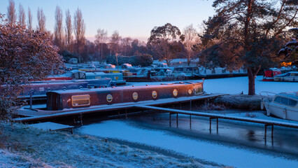 Unrecognisable Narrowboat in a frozen marina in early morning golden hour sun after a light snowfall. © Steven F Granville