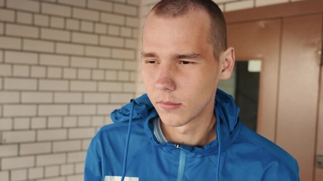 young white man wearing blue jacket adjusting hood, checking wet weather at brick doorway, crewcut hair, pensive expression, quiet urban mood, reflective solitude waiting in drizzle