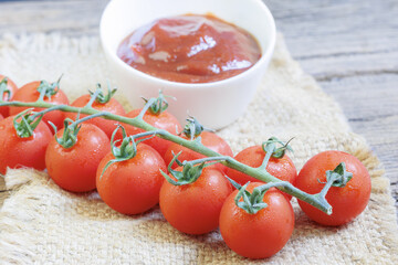 Fresh cherry tomatoes on vine rest on rustic cloth beside bowl of rich, red tomato sauce, creating vibrant and appetizing scene