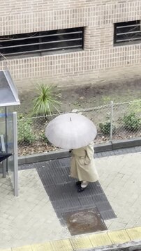 lluvia y temporal con hombre con paraguas y gabardina en parada de autob&uacute;s