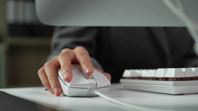 Close-up of a female office worker's hand moving and clicking a modern white computer mouse on a desk, with a mechanical keyboard visible nearby, symbolizing daily office tasks and workflow